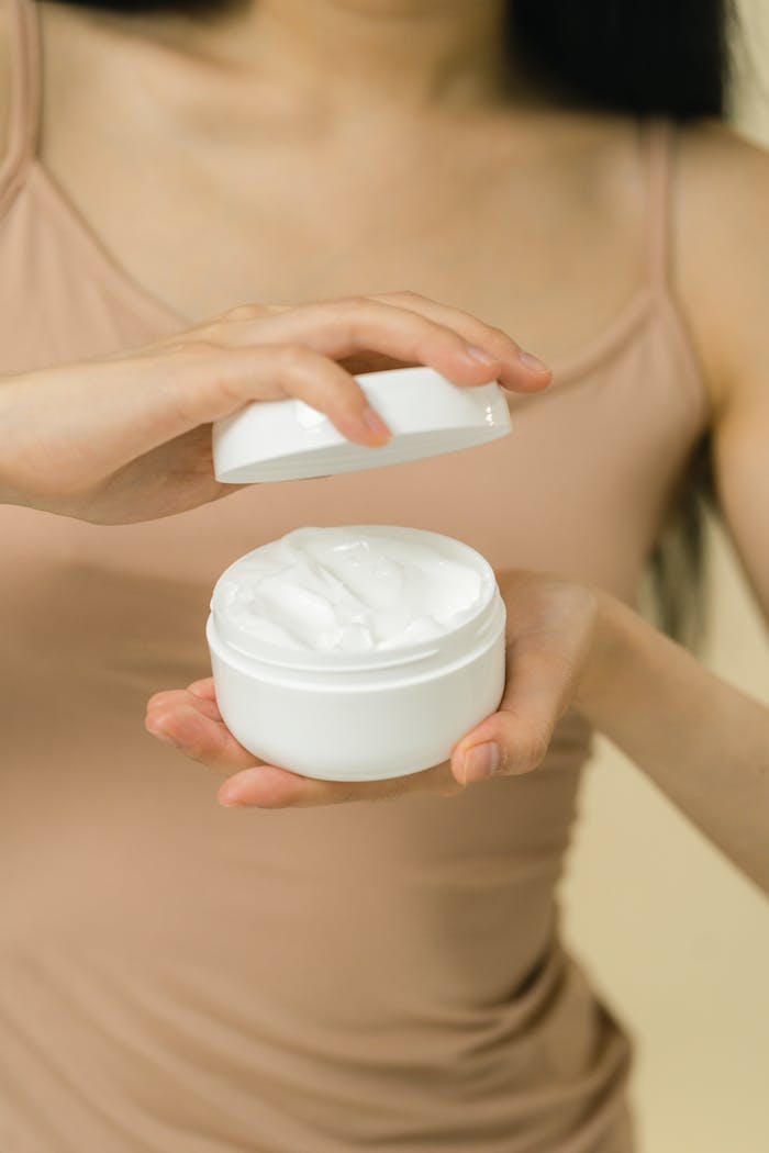 Close-up of a woman holding and opening a jar of cosmetic cream with soft focus.